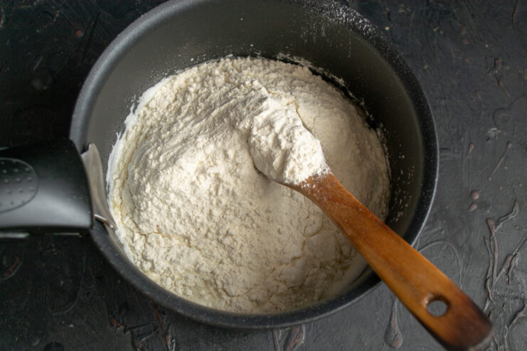 Stirring flour into the hot liquid Adding all-purpose flour into the hot milk mixture in a saucepan