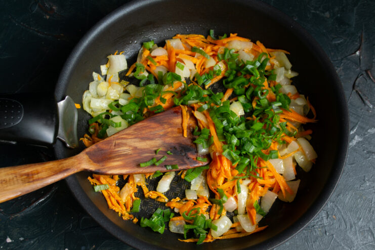 Adding green onions Mixing freshly chopped green onions into sautéed carrots and onions in a skillet.