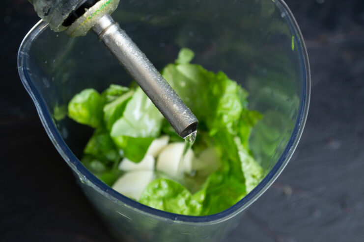 Adding Olive Oil Pouring extra virgin olive oil into a blender cup with fresh greens