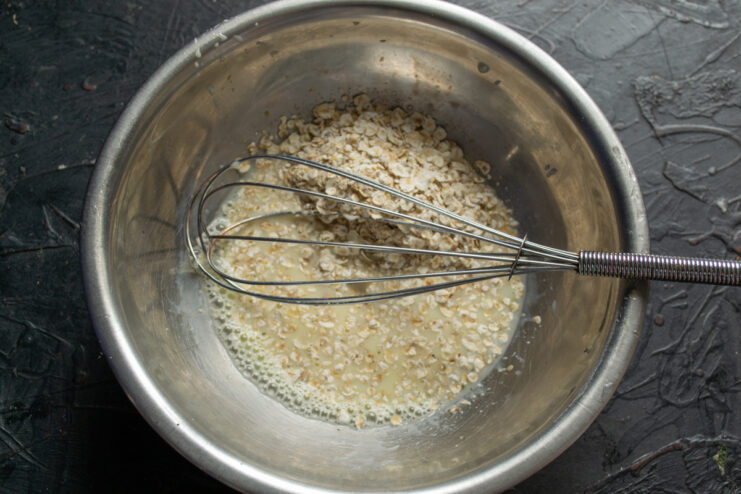 Adding Oats To The Batter Pouring quick-cooking rolled oats into the liquid egg mixture in a bowl