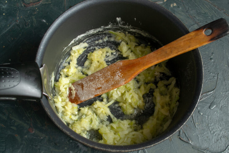 Adding flour to the base Sprinkling all-purpose flour over sauteed onions in a cooking pot