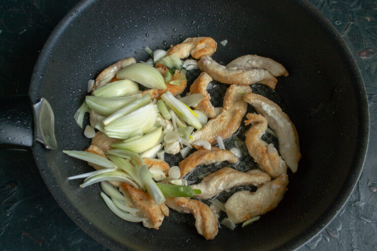 Adding vegetables to the meat Adding chopped onions to fried chicken in a pan