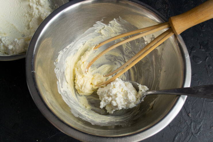 Adding sweetened ricotta to whipped butter in a mixing bowl.