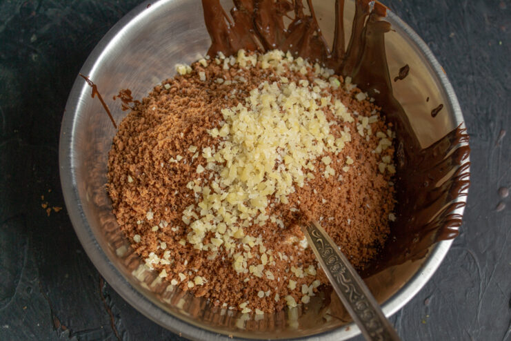 Adding chopped nuts to the chocolate mixture for petits fours.