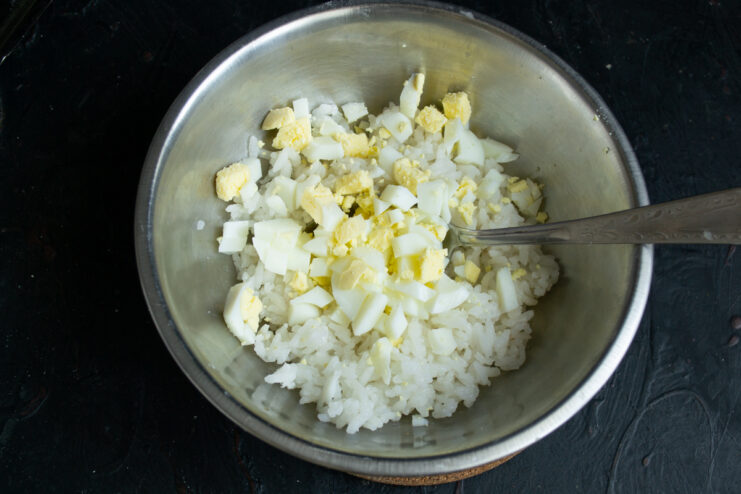 Adding chopped hard-boiled eggs to cooked rice in a bowl