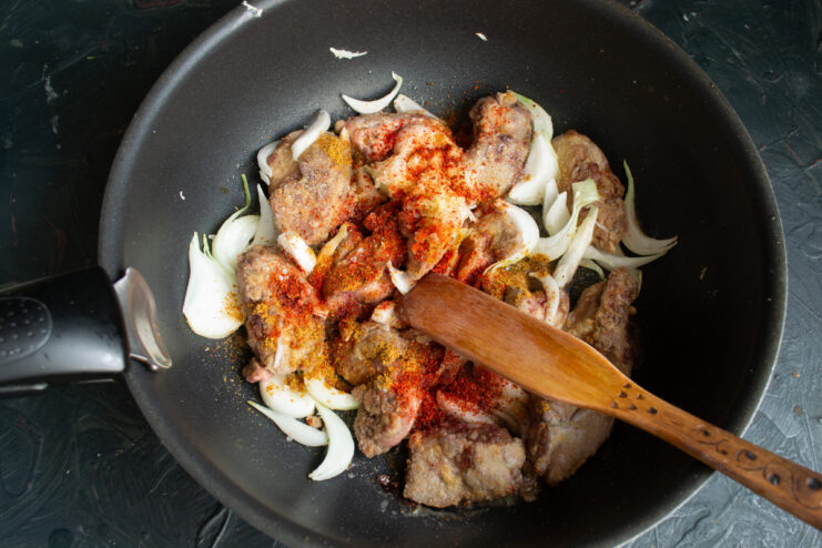 Spicing the Livers and Onions Chicken livers sautéing with onions, curry powder, and paprika in a pan