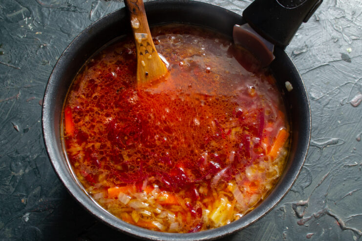 Adding the beet dressing Stirring the braised beet dressing into the pot of borscht