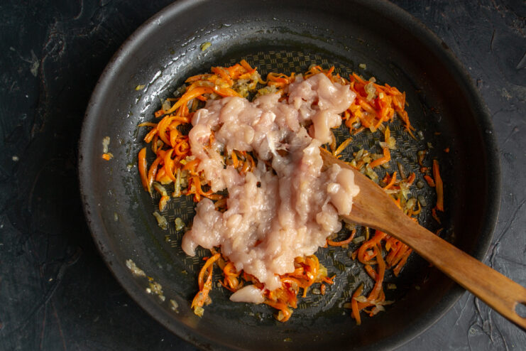 Adding chicken to the filling Adding raw ground chicken to the sauteed vegetables in a pan