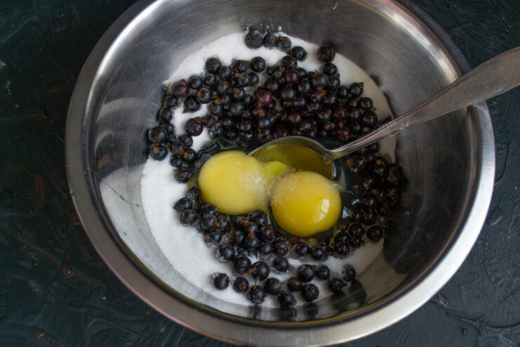 Adding Eggs To The Batter Adding raw cracked eggs into a bowl of blackcurrants and sugar