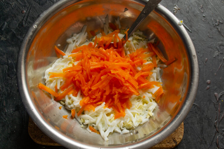 Adding grated boiled carrots to the eggs in a bowl.