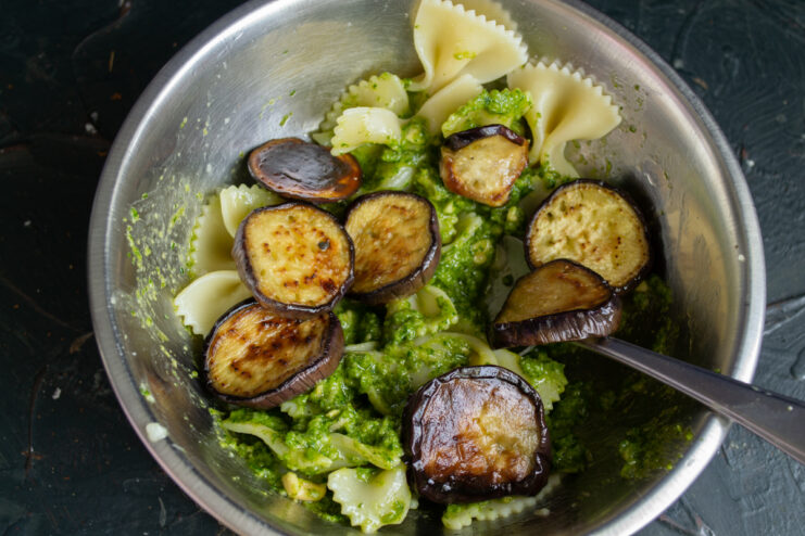 Combining the ingredients Adding golden fried eggplant rounds to the pesto pasta