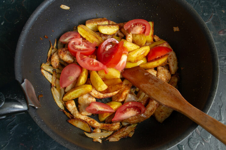 Adding fresh tomatoes Fresh tomato wedges placed on top of potatoes and chicken