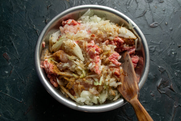 Preparing the meatball mixture Ground meat mixed with onions and spices in a metal bowl