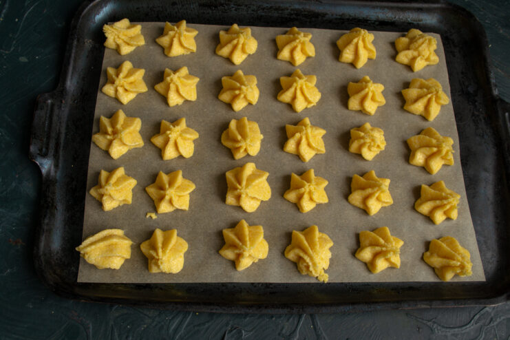 Piping the cookies Piped star-shaped polenta cookies on a parchment-lined baking sheet.