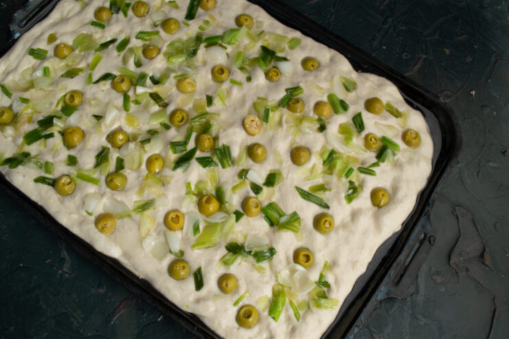Adding the topping Raw focaccia dough topped with onions and olives