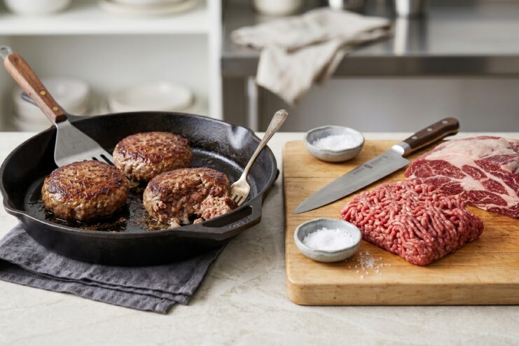 Perfectly ground meat and juicy cooked patties Juicy cooked meat patties in a skillet alongside fresh ground meat on a wooden cutting board.