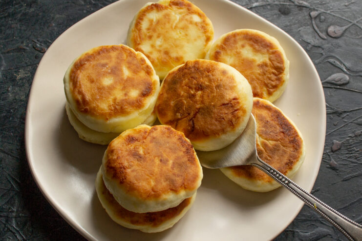 Fried syrniki plated on a white dish with a kitchen spatula