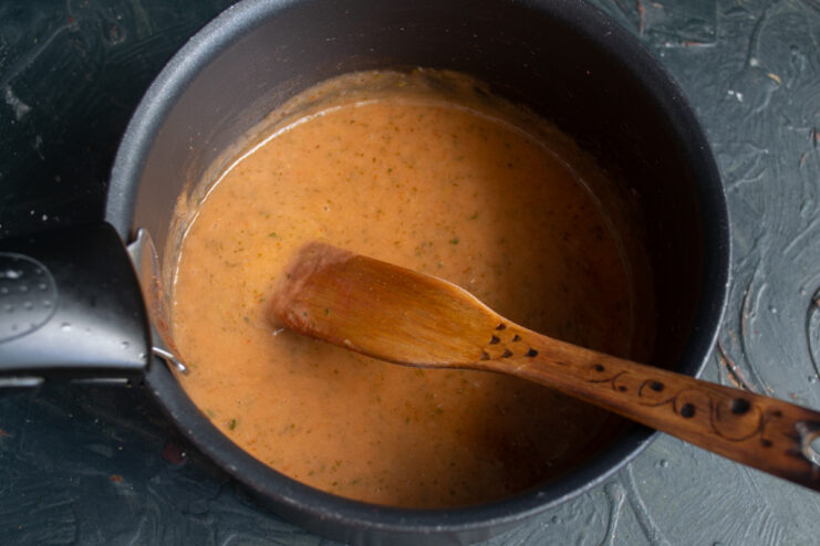 Pouring potato starch slurry in a thin stream into boiling sauce while stirring constantly