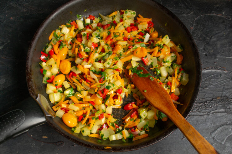 Cooked vegetable ratatouille in a skillet mixed with fresh herbs.