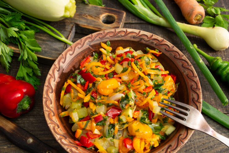 Finished zucchini ratatouille in a clay bowl on a wooden background with fresh ingredients.