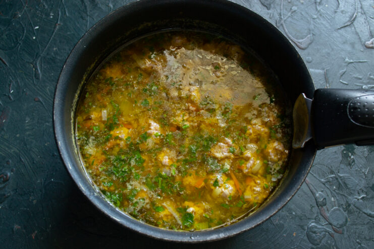 Final cooking stage Finished meatball soup with fresh herbs in a cooking pot