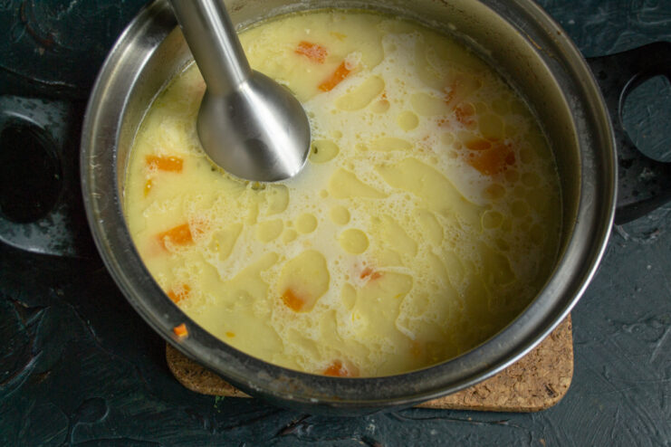 Blending the cooked vegetable soup with an immersion blender until smooth
