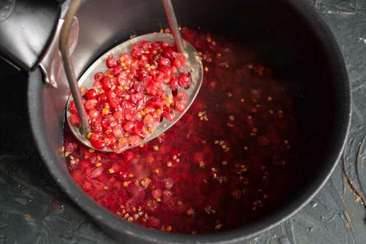 Mashing boiled redcurrants with a potato masher in a saucepan to create a rich base