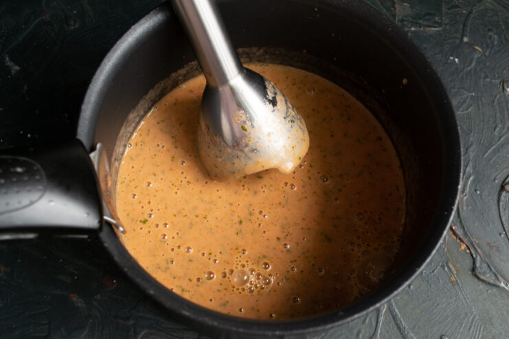 Blending the redcurrant sauce with an immersion blender to achieve a smooth creamy consistency