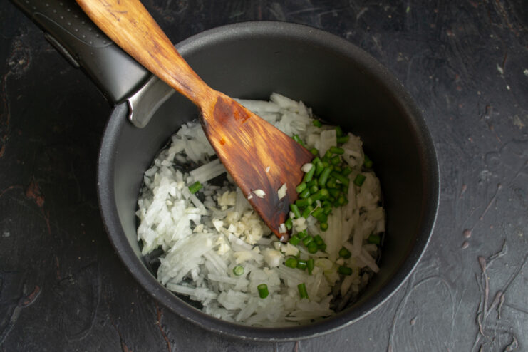 Adding garlic scapes Chopped garlic scapes and minced garlic added to a pot.
