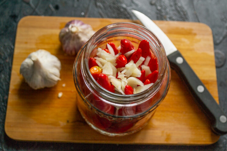 Adding the garlic Finely chopped garlic sprinkled over chili peppers in a jar