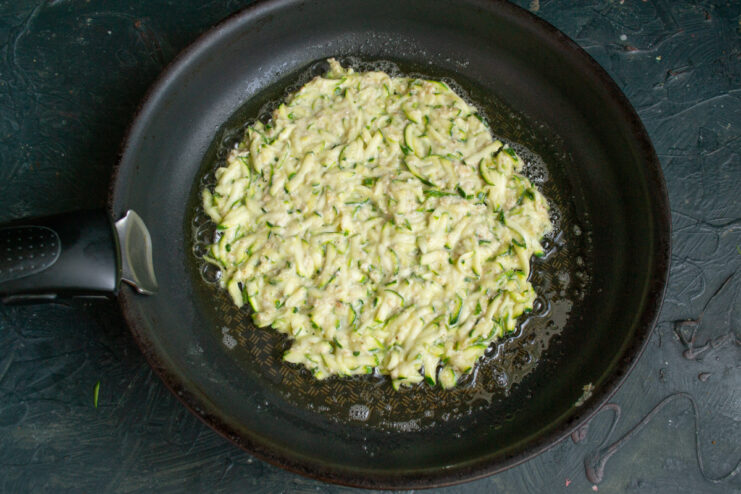 Frying the zucchini base Spreading zucchini batter evenly in a hot frying pan.
