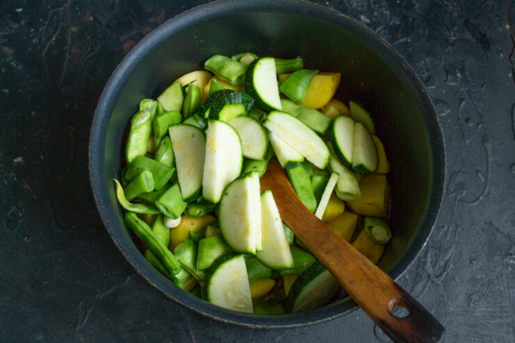 Diced potatoes, green beans, and sliced zucchini cooking in a pot