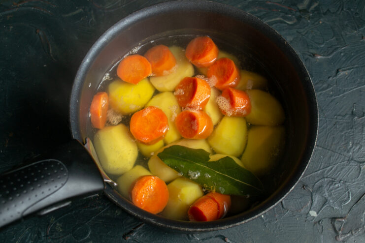 Parboiling the Vegetables Potatoes and carrots boiling in a pot of water with a bay leaf.