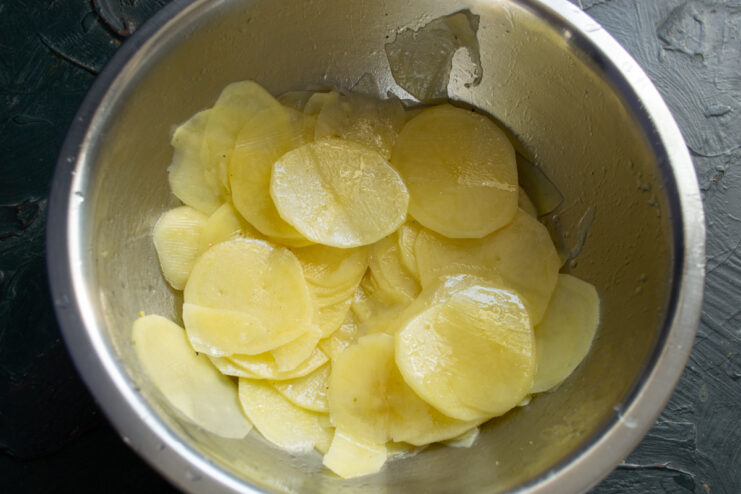 Seasoning the potatoes Sliced potatoes mixed with olive oil and spices in a bowl