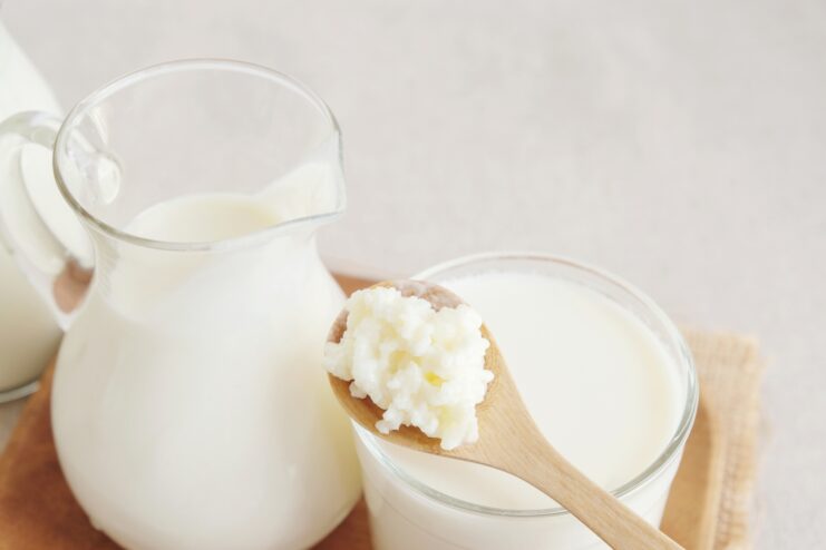 Kefir grains resting on a wooden spoon held over a glass of fresh kefir.