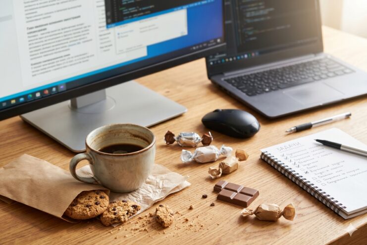 Sugar snack during work Coffee, cookies, and chocolate on a desk next to a laptop