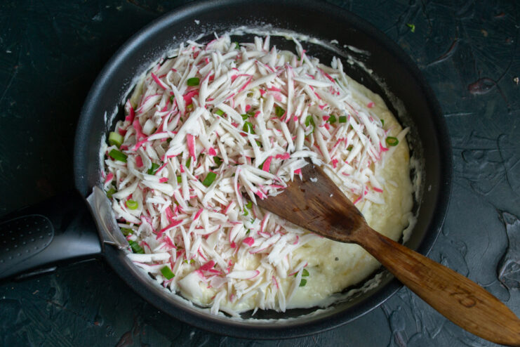 Combining filling and sauce Imitation crab sticks added to the melted cheese sauce in a pan