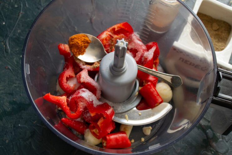 Adding Spices and Salt Coarse sea salt and ground paprika sprinkled over chopped vegetables in a processor.