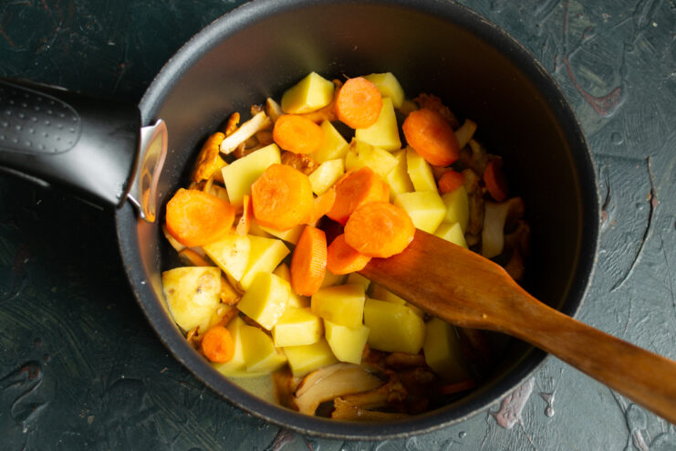 Adding the carrots Sliced carrot rounds on top of potatoes and chanterelles in a pan