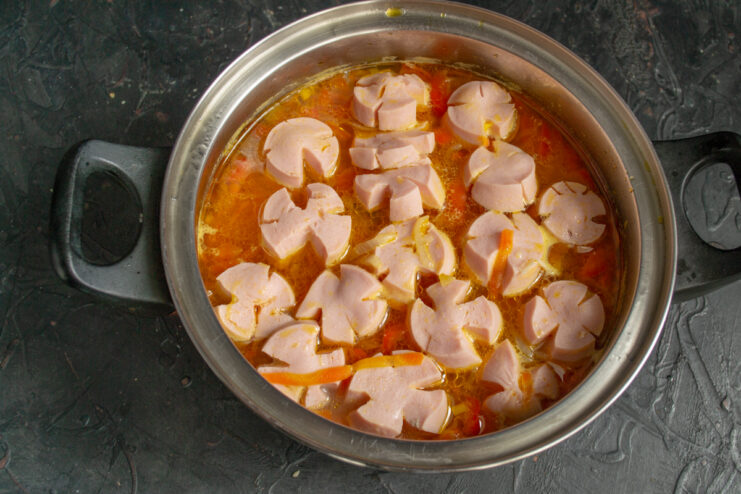 Adding sliced sausage Scored cooked sausage slices boiling in the rich soup broth