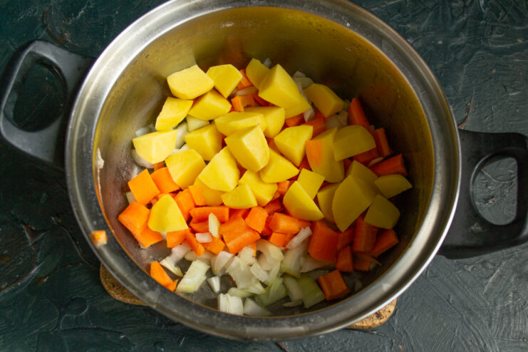 Cubed potatoes added to the onions and carrots inside the pot