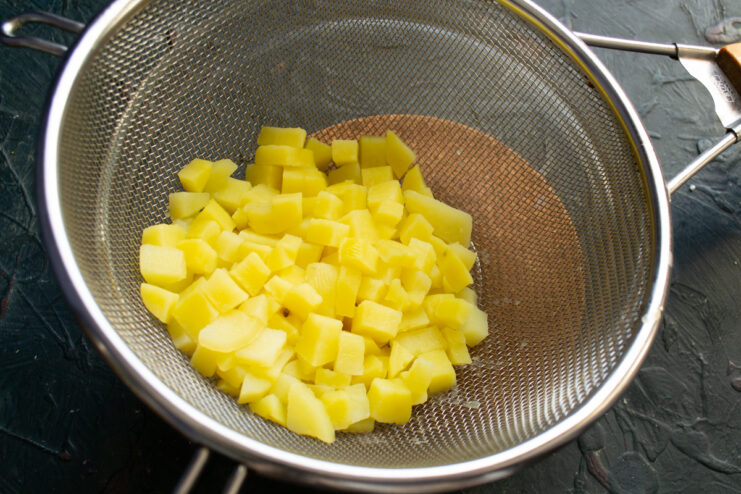 Preparing the potatoes Cubed boiled potatoes resting in a metal sieve