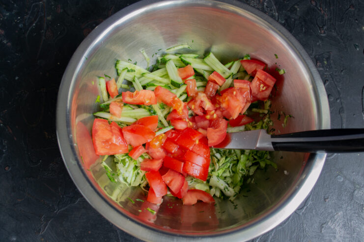 Adding Diced Tomatoes Small cubes of fresh red tomatoes placed over julienned cucumbers and cabbage in a bowl.