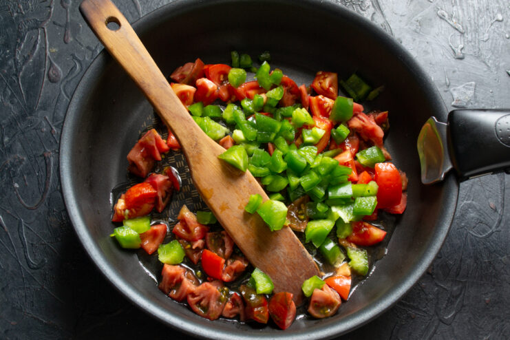 Adding diced green bell pepper to the tomatoes in a skillet
