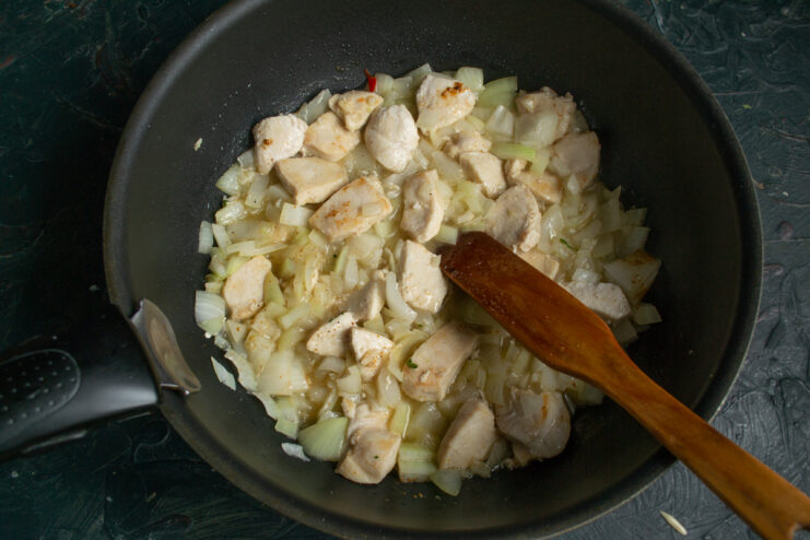 Cooking diced onion with chicken pieces in a skillet