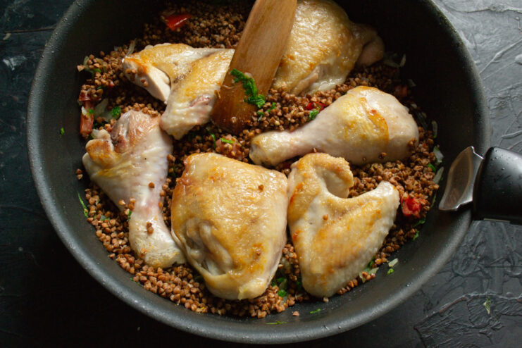 Assembling the Dish Before Baking Chicken pieces arranged on top of buckwheat and vegetables