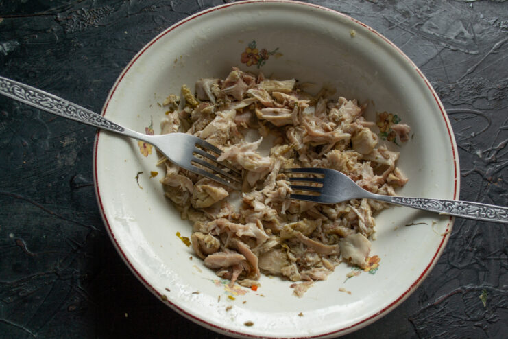 Shredding the chicken meat Shredding tender boiled chicken meat into fine strands using two forks