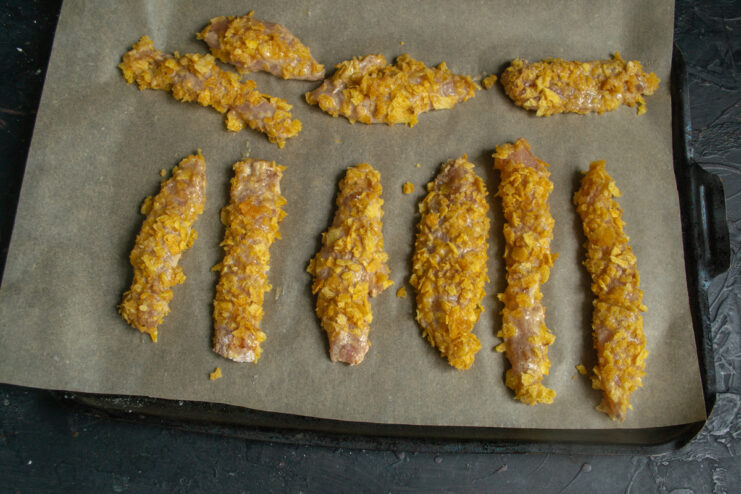 Arranging strips on the baking sheet Raw breaded chicken strips arranged on a parchment-lined baking sheet