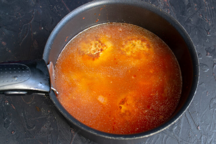 Pouring Broth Into The Soup Chicken broth being poured into a pot with tomatoes and meatballs.