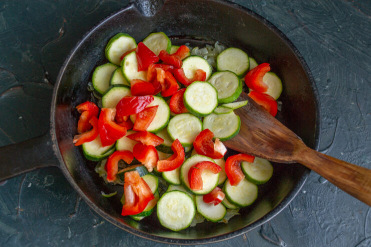 Adding the Red Bell Pepper Diced red bell pepper simmering with zucchini and onions in a pan